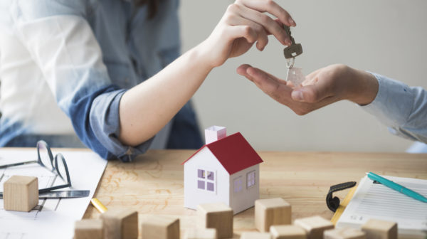 close-up-woman-s-hand-giving-house-key-man-wooden-table